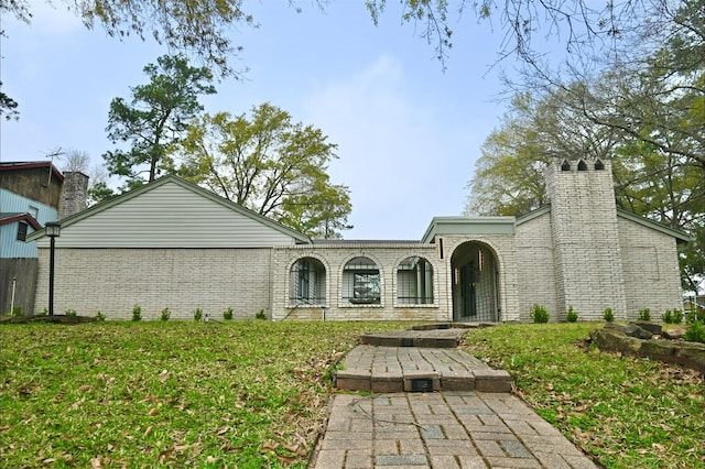 view of front of house featuring brick siding, a front yard, and a chimney