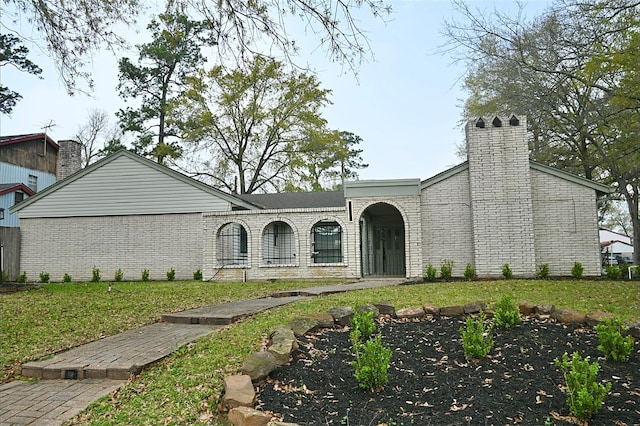 view of front of home featuring brick siding, a chimney, and a front yard