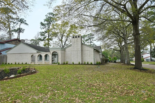 view of front facade with brick siding, a chimney, and a front lawn