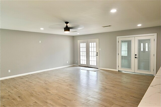 interior space with baseboards, visible vents, light wood finished floors, ceiling fan, and french doors