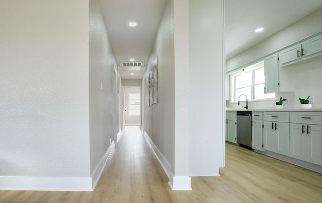 hall with visible vents, baseboards, light wood-type flooring, a textured wall, and a sink