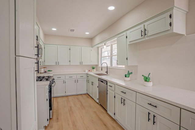 kitchen with light wood finished floors, a sink, appliances with stainless steel finishes, light countertops, and decorative backsplash