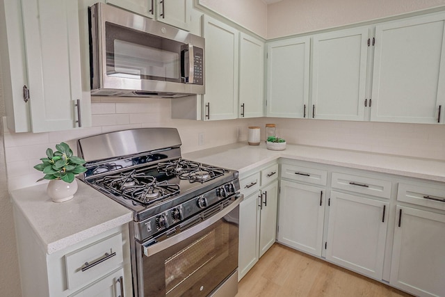 kitchen featuring light wood-style flooring, stainless steel appliances, decorative backsplash, light countertops, and white cabinetry