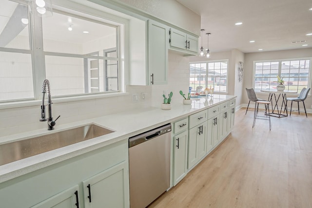 kitchen featuring light wood-type flooring, a sink, stainless steel dishwasher, light countertops, and decorative backsplash