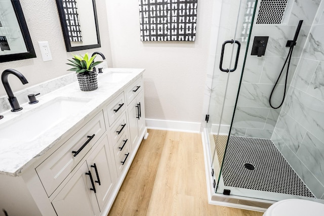 bathroom featuring a sink, a marble finish shower, baseboards, and wood finished floors