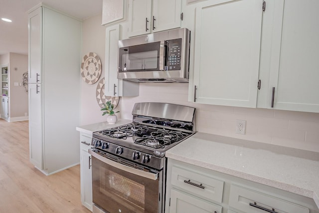 kitchen featuring black gas range oven, light wood-style flooring, white cabinetry, stainless steel microwave, and backsplash