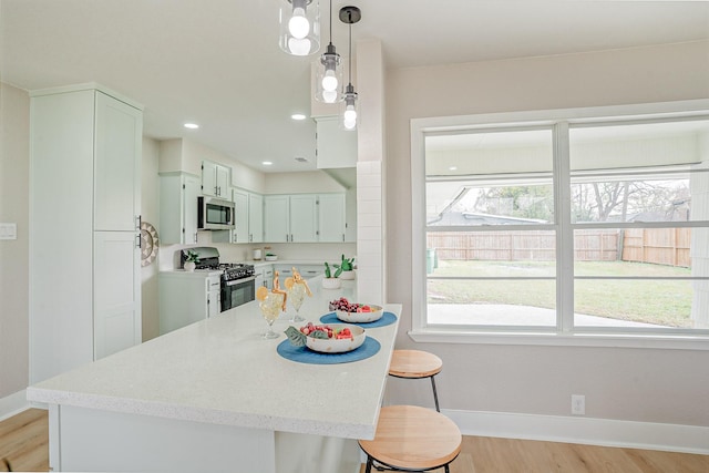 kitchen with baseboards, a breakfast bar, hanging light fixtures, appliances with stainless steel finishes, and light wood-type flooring