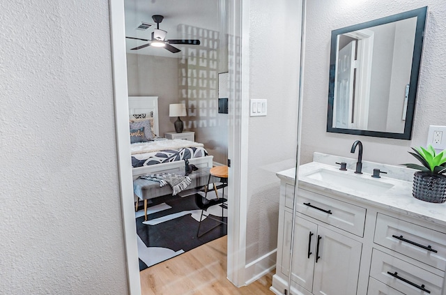 ensuite bathroom with vanity, wood finished floors, visible vents, a ceiling fan, and a textured wall