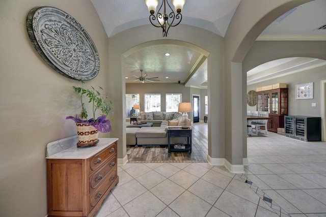 foyer entrance with baseboards, vaulted ceiling, light tile patterned floors, ceiling fan with notable chandelier, and arched walkways