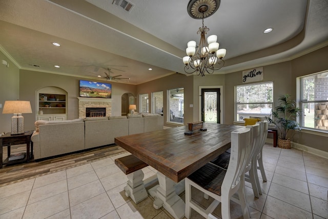 dining area featuring light tile patterned floors, visible vents, a tray ceiling, crown molding, and ceiling fan with notable chandelier