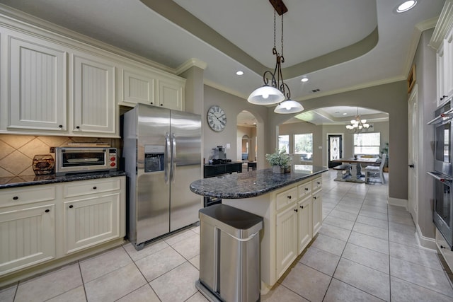 kitchen featuring a center island, a chandelier, a tray ceiling, appliances with stainless steel finishes, and arched walkways