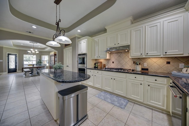 kitchen featuring a notable chandelier, under cabinet range hood, a tray ceiling, stainless steel appliances, and arched walkways