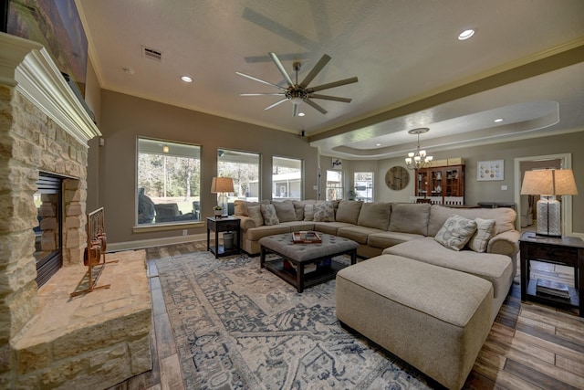 living area with visible vents, crown molding, a stone fireplace, ceiling fan with notable chandelier, and wood finished floors