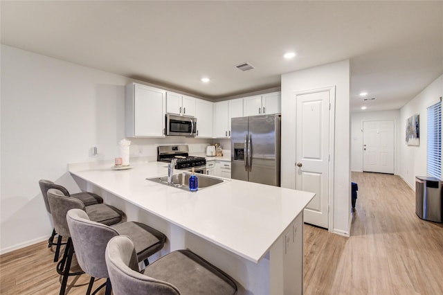 kitchen featuring a peninsula, light wood-style flooring, stainless steel appliances, light countertops, and a kitchen breakfast bar