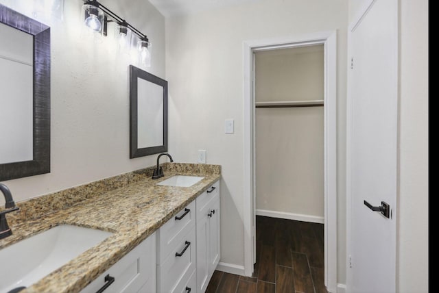 bathroom featuring double vanity, baseboards, wood finish floors, and a sink