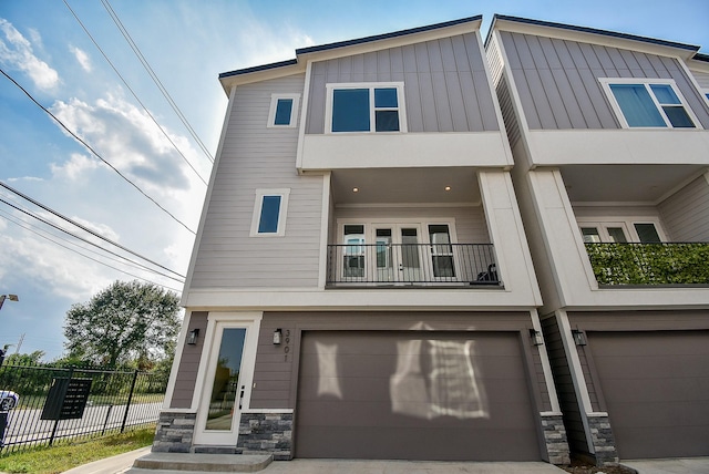 view of front facade with stone siding, an attached garage, a balcony, and fence