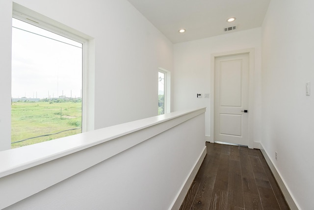 corridor featuring dark wood-style floors, visible vents, baseboards, recessed lighting, and an upstairs landing