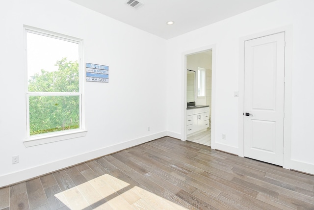 unfurnished bedroom featuring ensuite bath, baseboards, visible vents, and light wood-type flooring