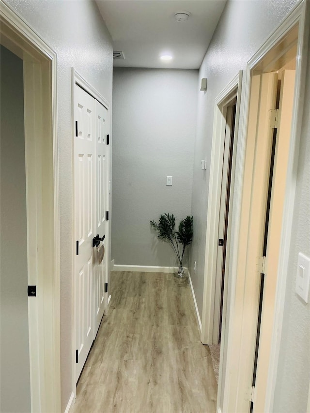 hall with baseboards, visible vents, and light wood finished floors