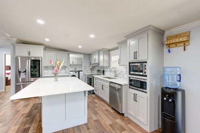 kitchen featuring backsplash, a kitchen island, washing machine and dryer, stainless steel appliances, and a sink