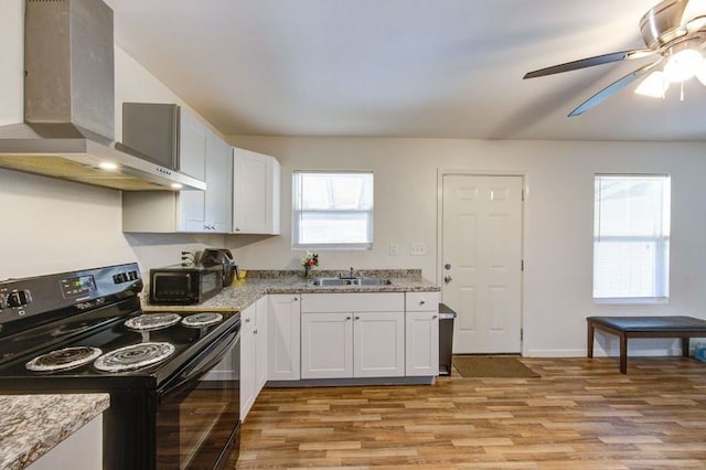 kitchen featuring light wood finished floors, black electric range, white cabinetry, wall chimney exhaust hood, and a sink