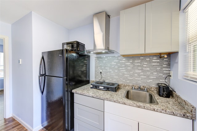 kitchen featuring freestanding refrigerator, a sink, cooktop, wall chimney exhaust hood, and tasteful backsplash