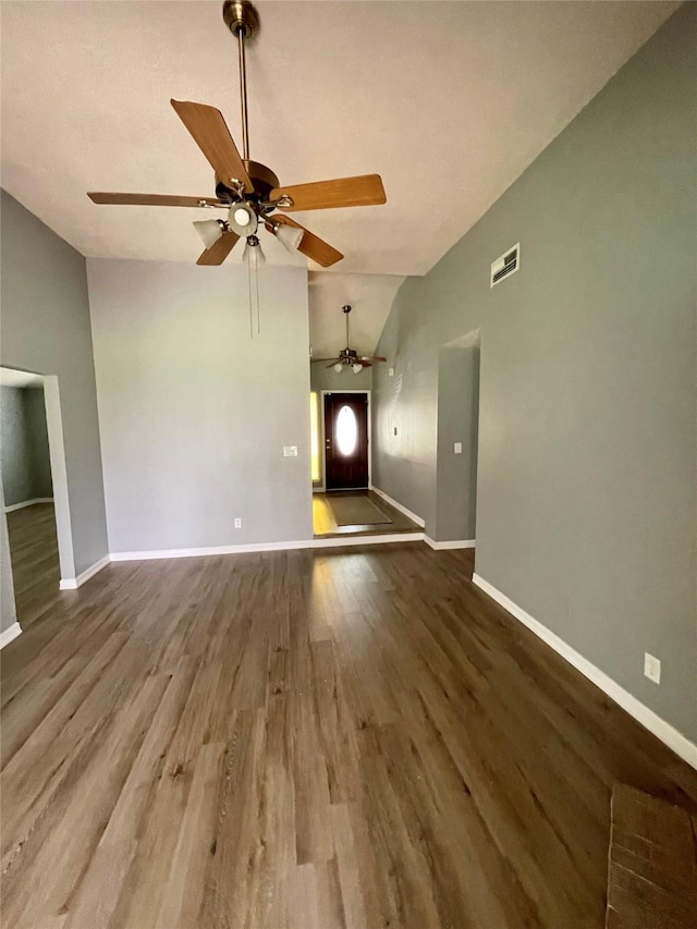 unfurnished living room featuring wood finished floors, a ceiling fan, visible vents, baseboards, and vaulted ceiling