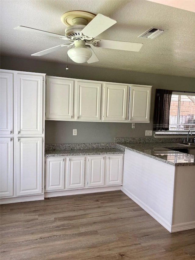 kitchen with a sink, visible vents, wood finished floors, and white cabinetry