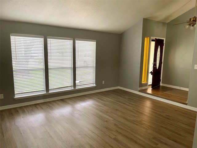 empty room with dark wood-style floors, a ceiling fan, baseboards, and vaulted ceiling