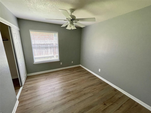 unfurnished bedroom with a ceiling fan, a textured ceiling, wood finished floors, a closet, and baseboards