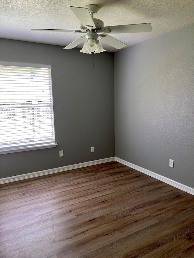 unfurnished room with a textured ceiling, dark wood-style floors, baseboards, and ceiling fan