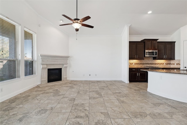 8022 Duncan Ranch Ln, Richmond, TX 77407 - kitchen with stainless steel microwave, a ceiling fan, backsplash, dark brown cabinetry, and a premium fireplace