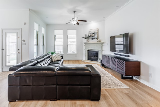 living area featuring ornamental molding, a glass covered fireplace, wood finished floors, baseboards, and ceiling fan