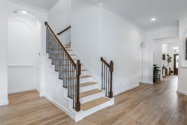 staircase with wood finished floors, baseboards, recessed lighting, arched walkways, and ornamental molding