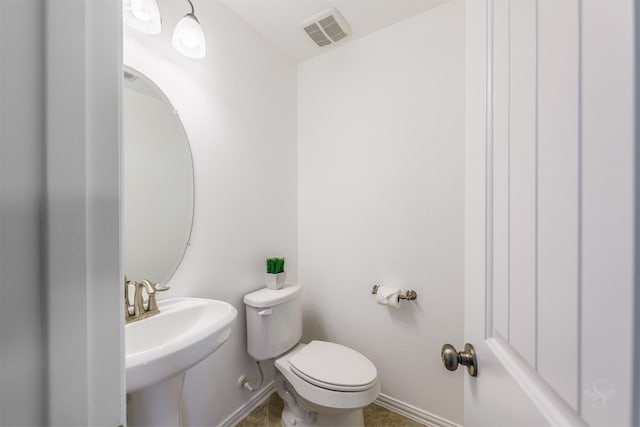 half bath with visible vents, toilet, baseboards, and a sink