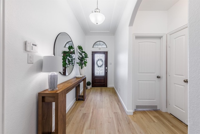 foyer featuring arched walkways, baseboards, and light wood-style floors