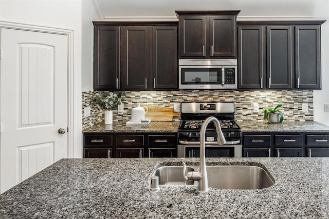 kitchen with dark stone countertops, a sink, ornamental molding, stainless steel appliances, and tasteful backsplash