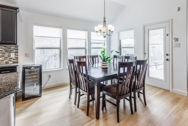 dining area with wine cooler, light wood-type flooring, lofted ceiling, ornamental molding, and a notable chandelier