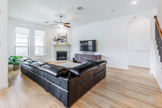 living room featuring a glass covered fireplace, stairway, light wood-type flooring, and ceiling fan