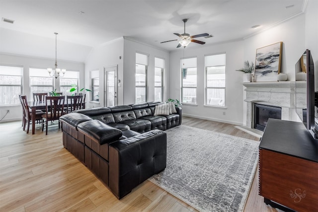 living area with a healthy amount of sunlight, light wood finished floors, a premium fireplace, ornamental molding, and ceiling fan with notable chandelier