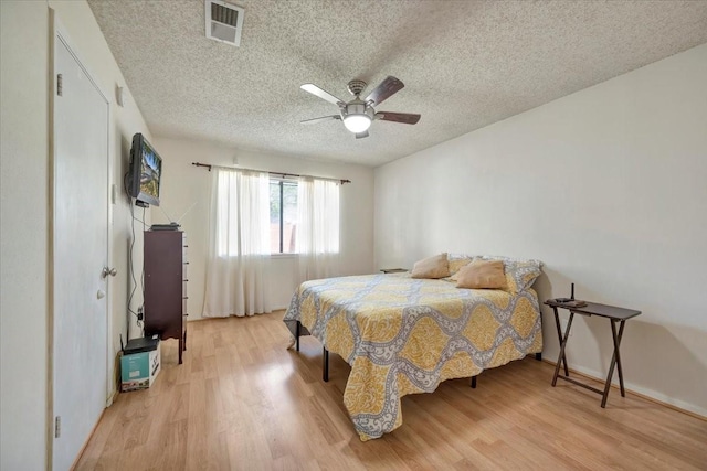 bedroom with visible vents, a textured ceiling, light wood finished floors, baseboards, and ceiling fan