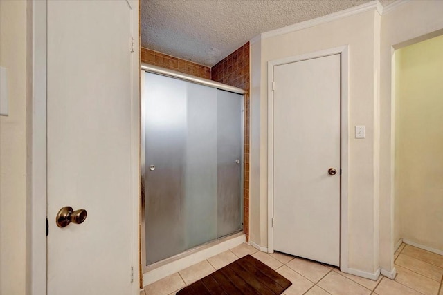 bathroom featuring ornamental molding, a textured ceiling, a shower stall, tile patterned flooring, and baseboards