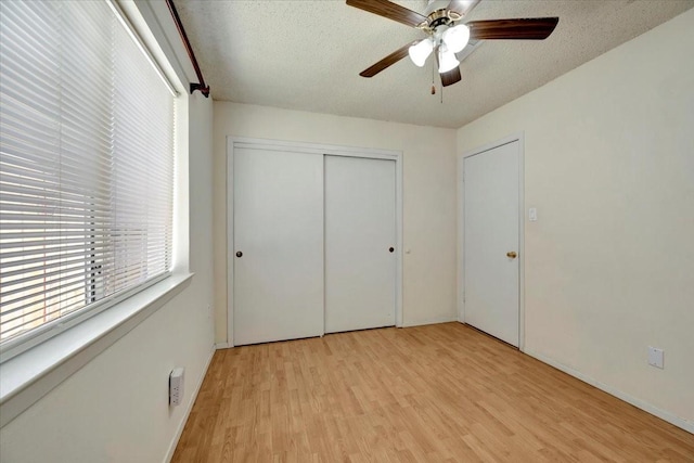 unfurnished bedroom with light wood-type flooring, a textured ceiling, a closet, and a ceiling fan