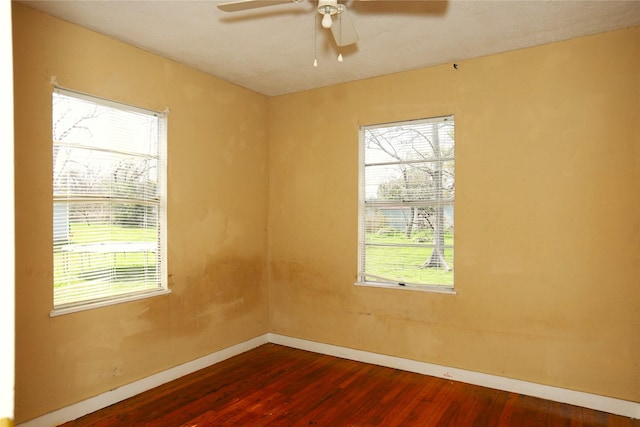 empty room featuring a ceiling fan, a healthy amount of sunlight, dark wood finished floors, and baseboards