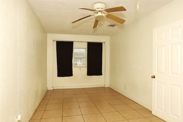 empty room with visible vents, a ceiling fan, a textured ceiling, light tile patterned floors, and baseboards