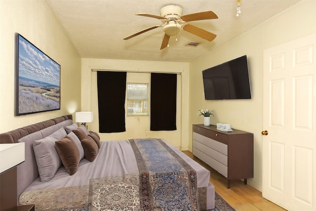 bedroom featuring visible vents, a textured ceiling, light wood-type flooring, and a ceiling fan