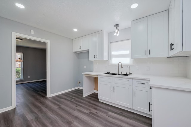 kitchen with tasteful backsplash, a sink, baseboards, white cabinets, and dark wood-style flooring