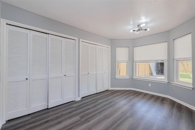 unfurnished bedroom with two closets, baseboards, dark wood finished floors, an inviting chandelier, and a textured ceiling