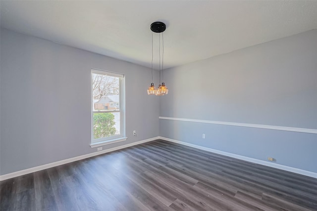 spare room with a notable chandelier, dark wood-type flooring, and baseboards