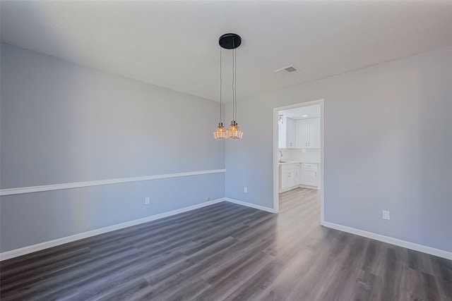 empty room with visible vents, baseboards, dark wood-style floors, a notable chandelier, and a sink